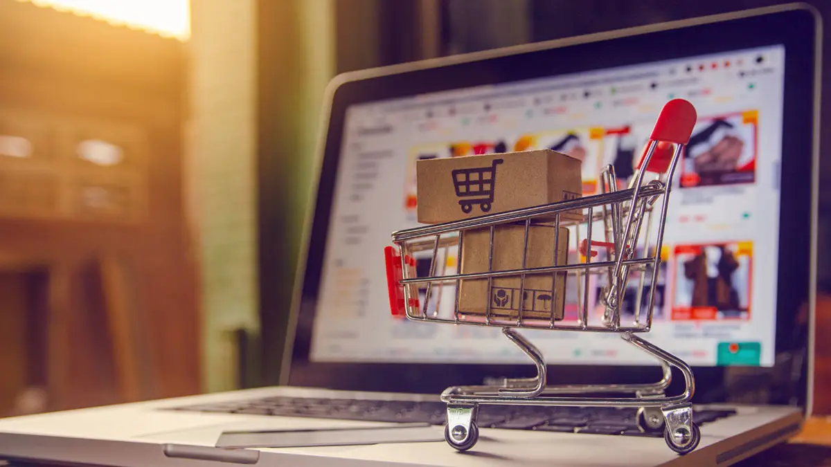 Miniature shopping cart with boxes on a laptop keyboard, symbolizing online shopping and home delivery.